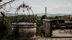 Une fontaine en pierre, surmontée d’une arche en métal, et une terrasse en bois avec des chaises.