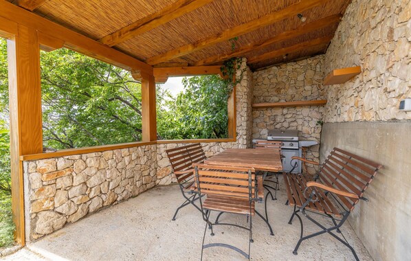 An outdoor patio with stone walls, wooden benches, and a grill.