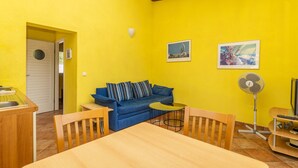 A bright yellow room with a blue sofa, a small round table, and a fan.