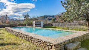 A rectangular stone pool with a stone wall surrounding it, a small stone building with a door, and a wooden fence in the background. - Cozy home in LE ROUET (LE ROUET)
