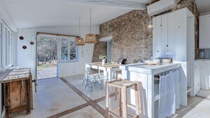 A spacious kitchen with a stone wall, white cabinetry, and a large window. - Cozy home in LE ROUET (LE ROUET)