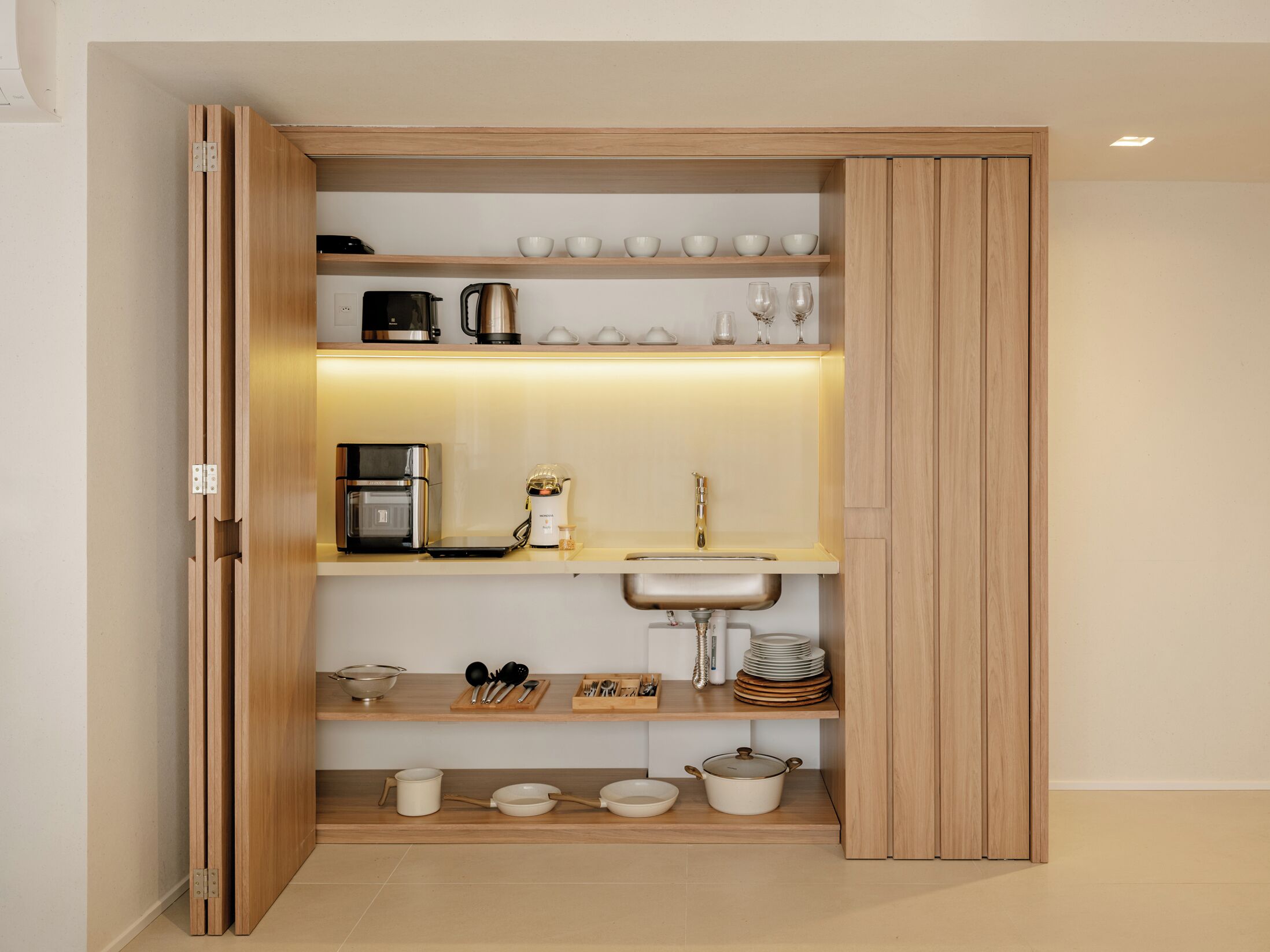 A kitchen with a built-in oven, coffee maker, sink, and various kitchenware on shelves.