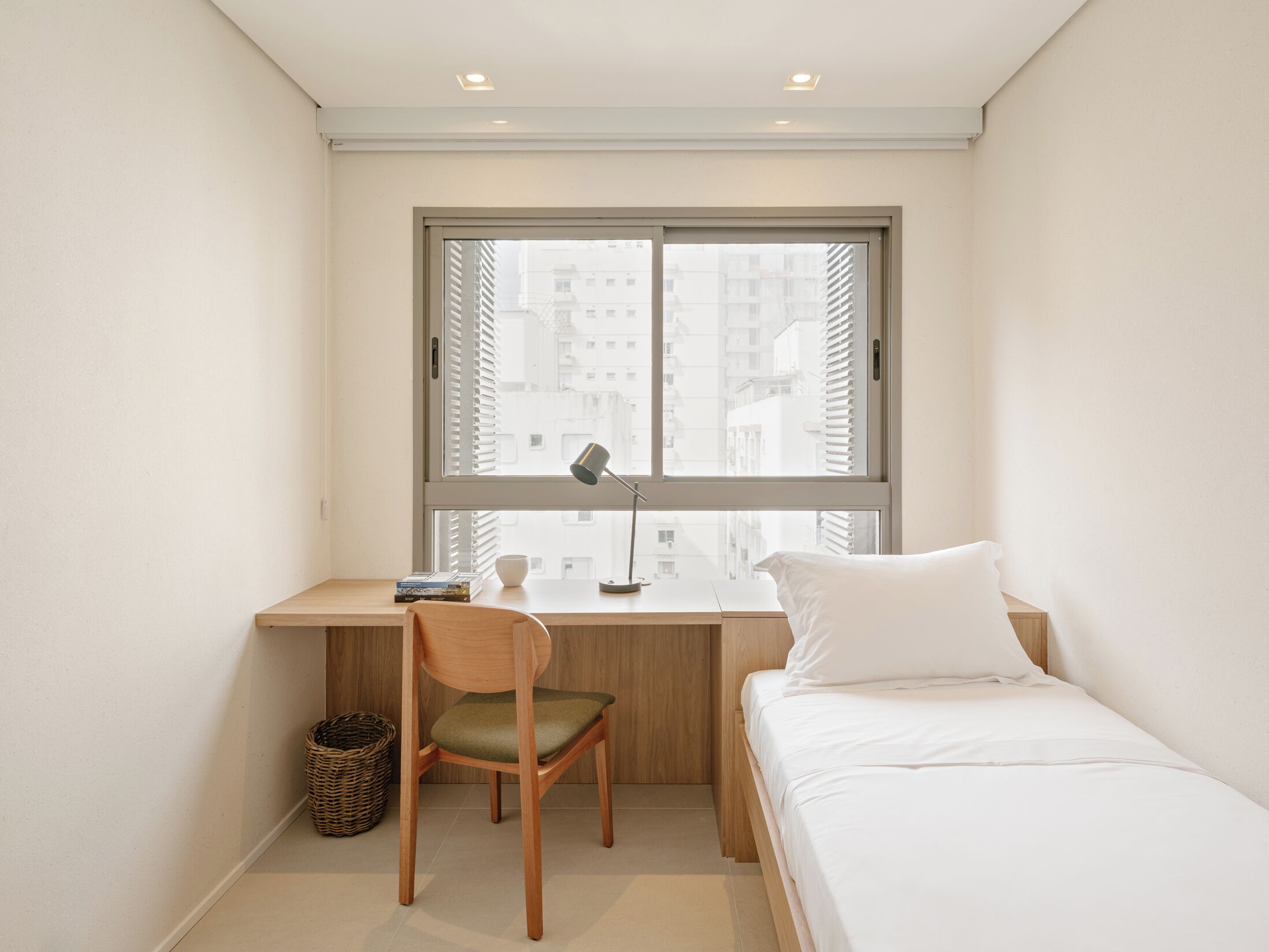 Quarto pequeno e moderno com uma cama de solteiro, uma escrivaninha e uma cadeira.