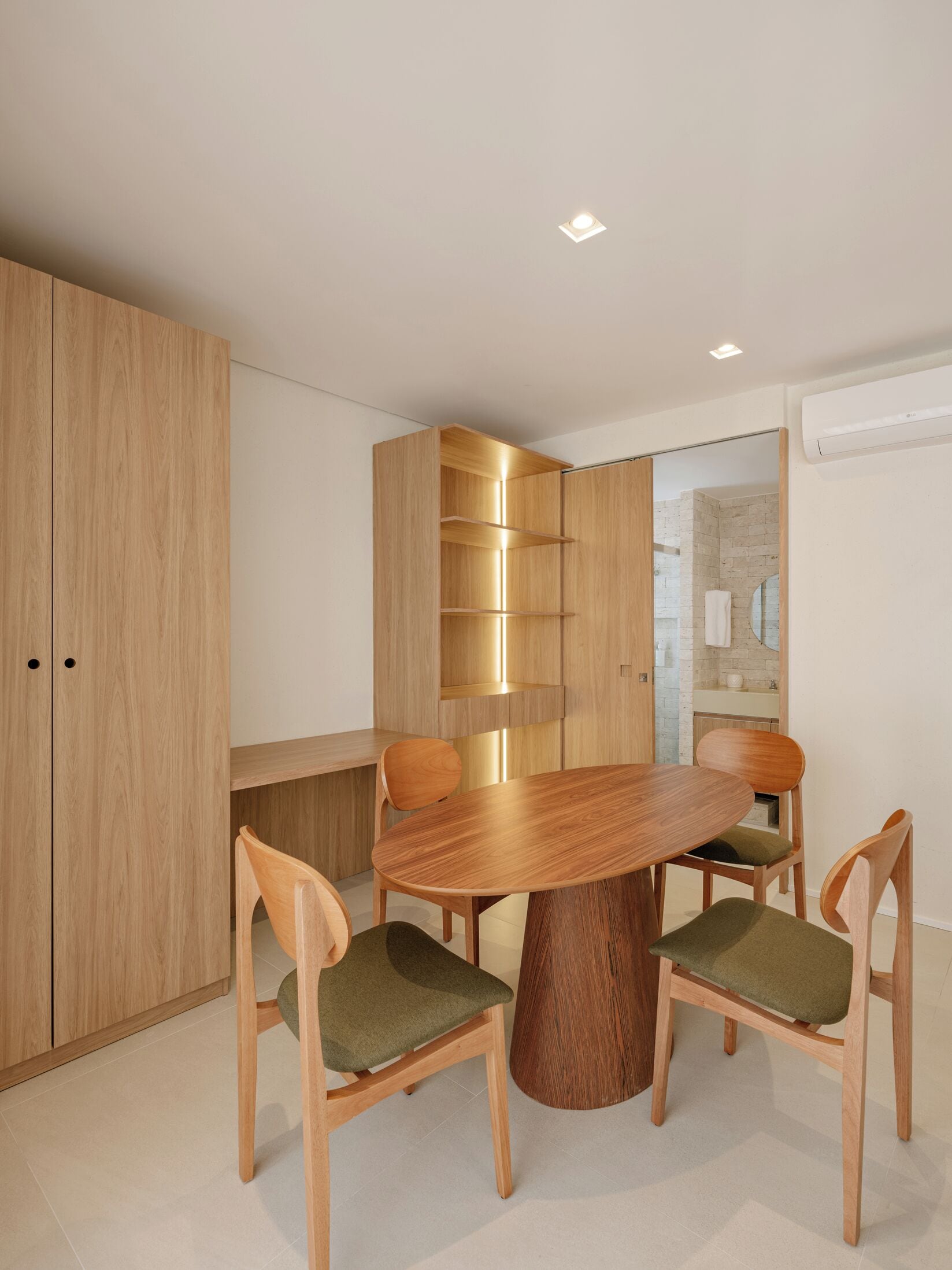 A modern dining area with a wooden table and chairs, a built-in bookshelf, and a visible bathroom in the background.