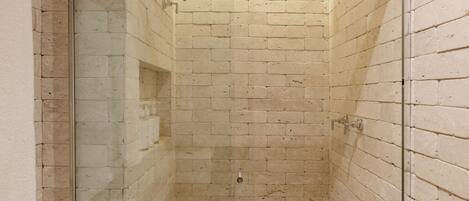 A modern bathroom with a glass-enclosed shower, beige brick walls, and a white ceiling.