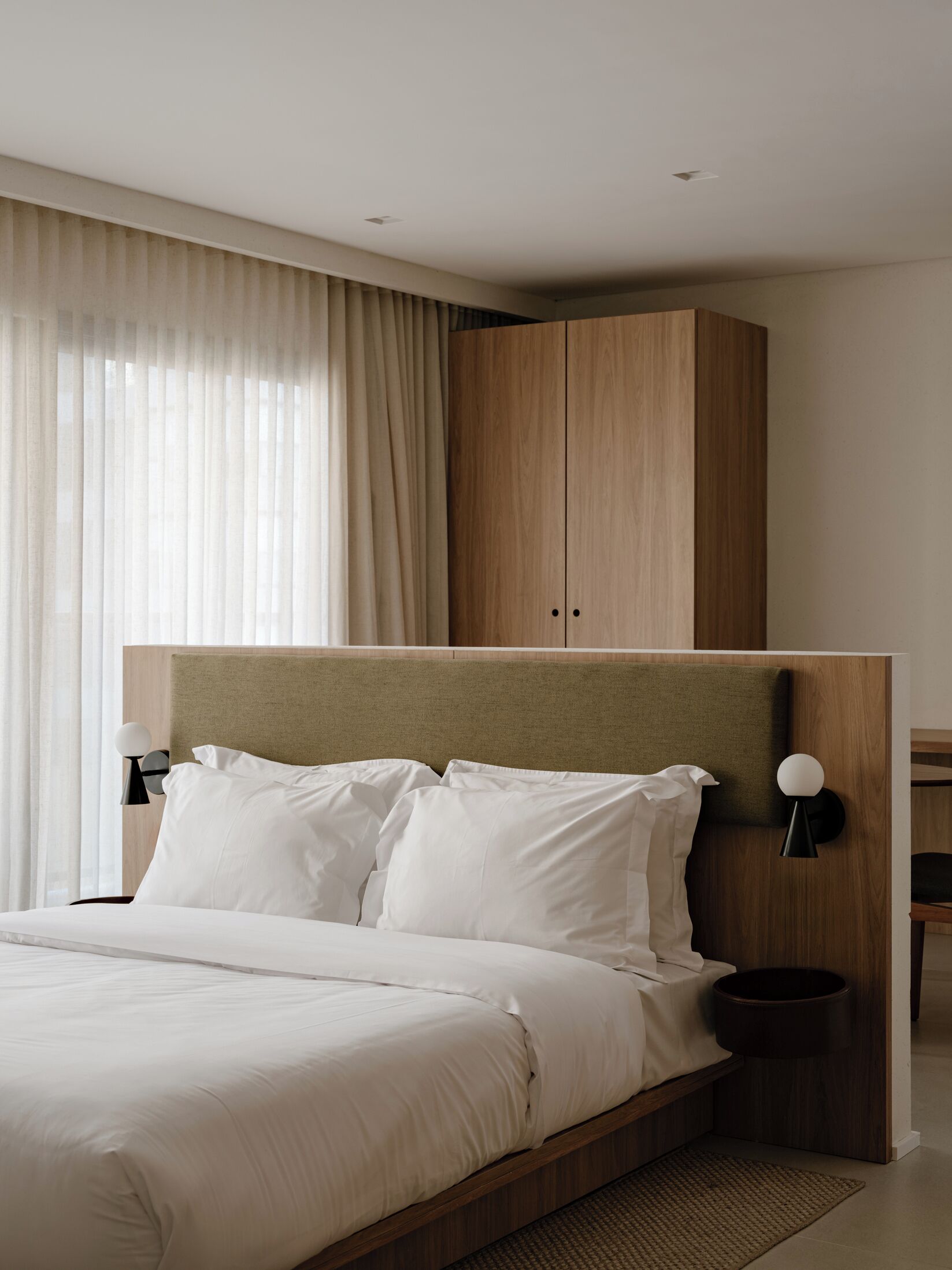 A modern hotel room with a large bed, wooden headboard, and a wardrobe.
