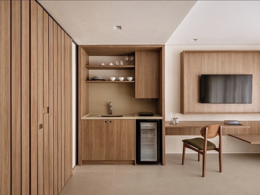 Una cocina moderna con armarios de madera, un refrigerador empotrado y un comedor con una silla.