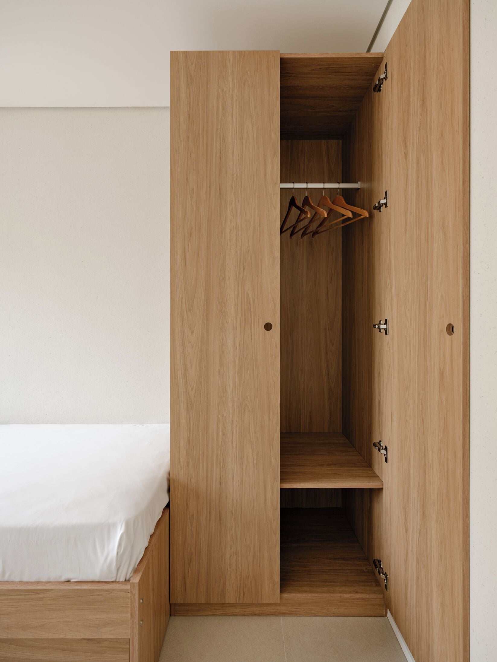 Un armario de madera con varias puertas, una barra para colgar ropa y una cama con colchón blanco.