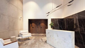 A modern reception area with a marble reception desk, white sofas, and a wooden door in the background. - Aloe Vila Nova Conceição (São Paulo)
