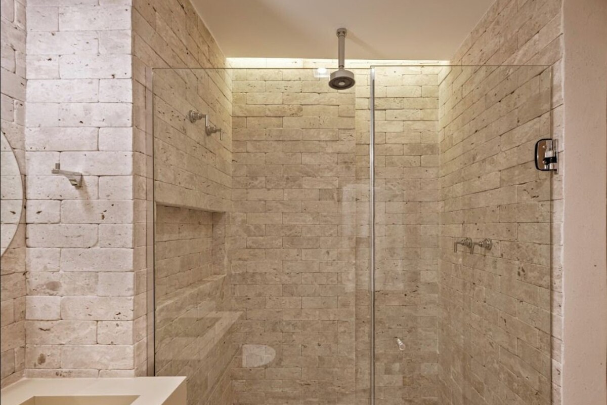 Un baño moderno con cabina de ducha de vidrio, lavamanos empotrado y pared con azulejos.
