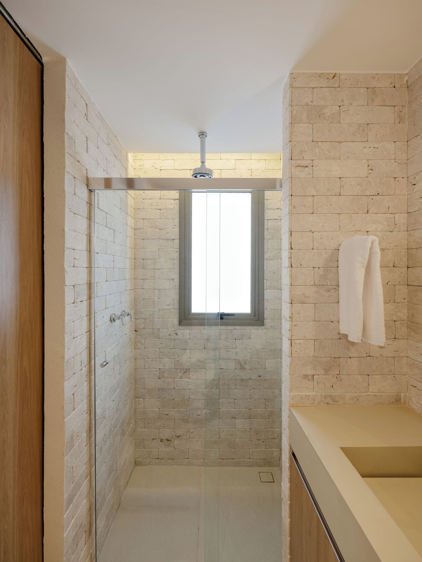Une petite salle de bain avec une fenêtre, une serviette accrochée au mur et une porte en bois.