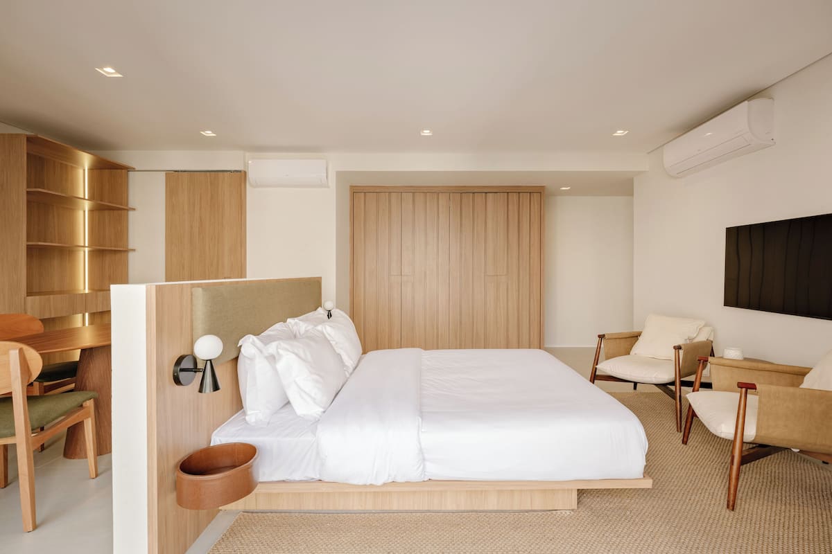 A modern bedroom with a large bed, wooden wardrobe, and two chairs.