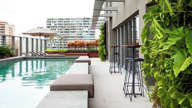 A modern outdoor pool area with a seating arrangement and a view of high-rise buildings in the background. - Aloe Vila Nova Conceição (São Paulo)