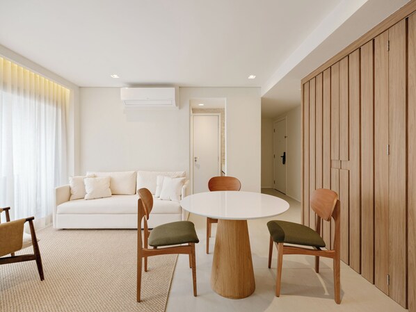 A modern living room with a white sofa, a round wooden table, and two chairs with green cushions.