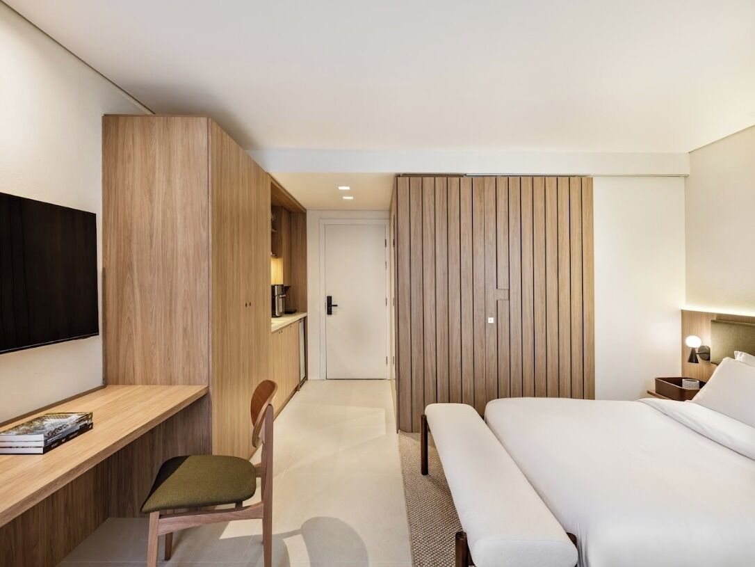 Una habitación de hotel moderna con un escritorio de madera, una cama, un televisor y un armario.