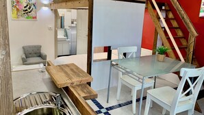 Et kompakt hotelværelse med køjeseng, lille tekøkken, spiseområde med glasbord og hvide stole samt en rød accentvæg.