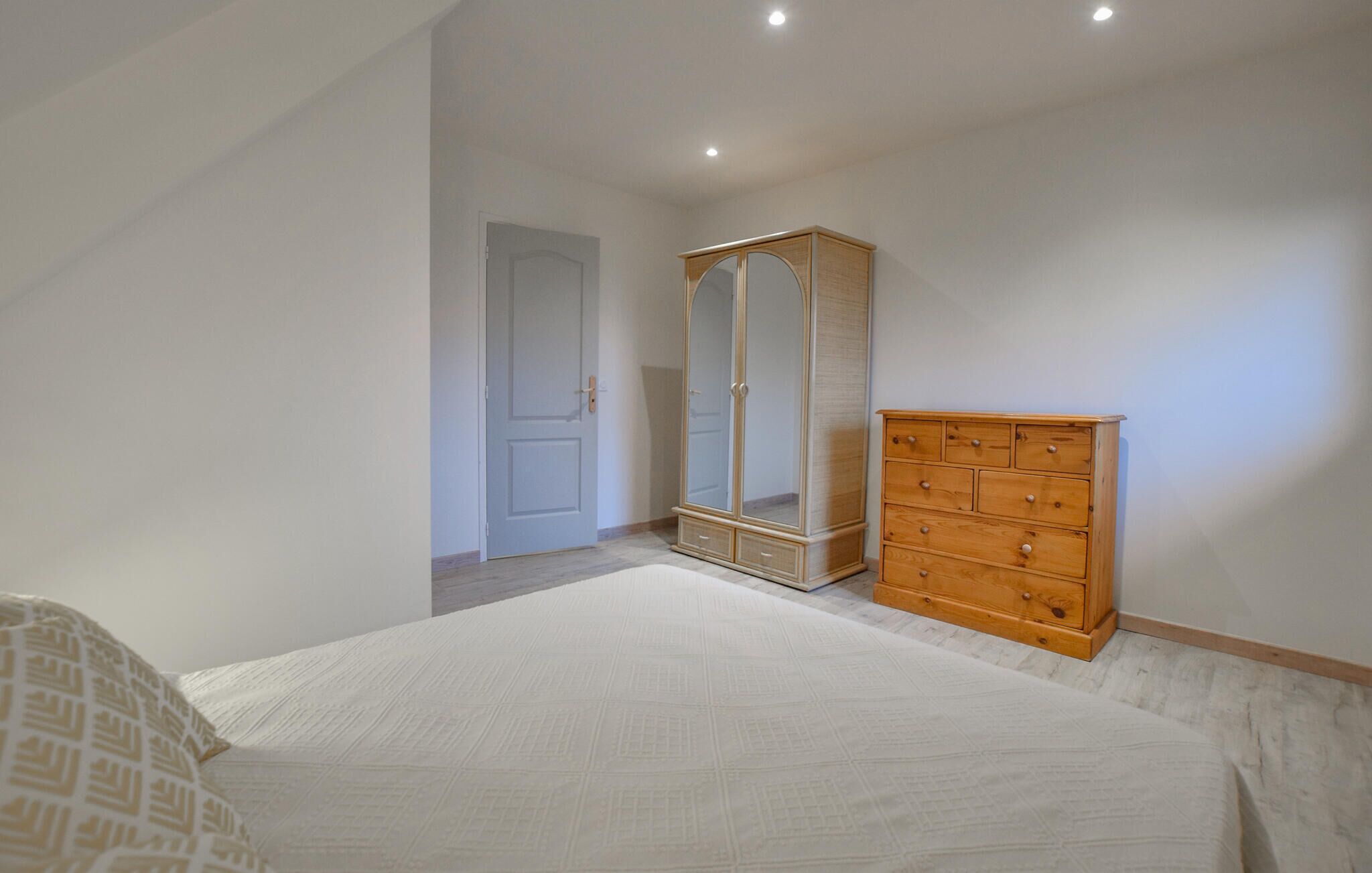 A bedroom with a bed, a wooden dresser, and a mirrored wardrobe.