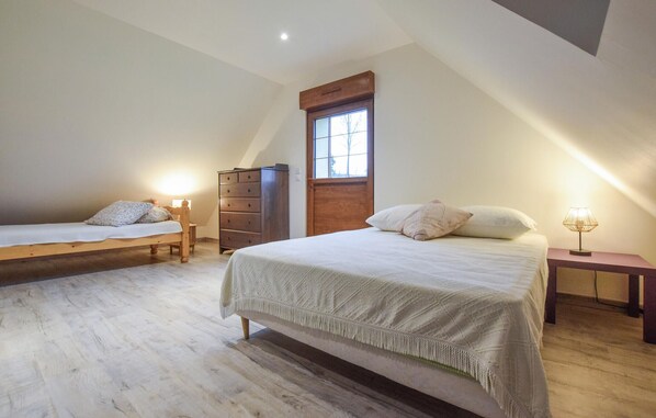 Une chambre avec deux lits, une commode en bois, une table de chevet et une fenêtre avec un volet en bois.