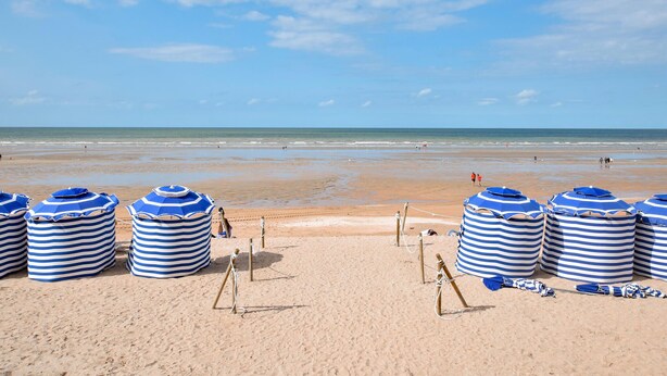 Ein Strand mit gestreiften Sonnenschirmen und Liegestühlen.