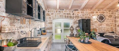 A rustic kitchen with stone walls, wooden beams, and a wooden dining table.