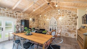 Un intérieur rustique avec un mur en pierre, des poutres en bois au plafond, une table à manger en bois et des chaises modernes.