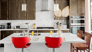 Una cocina moderna con armarios de madera oscura, una isla blanca con sillas rojas, electrodomésticos de acero inoxidable y lámparas colgantes.