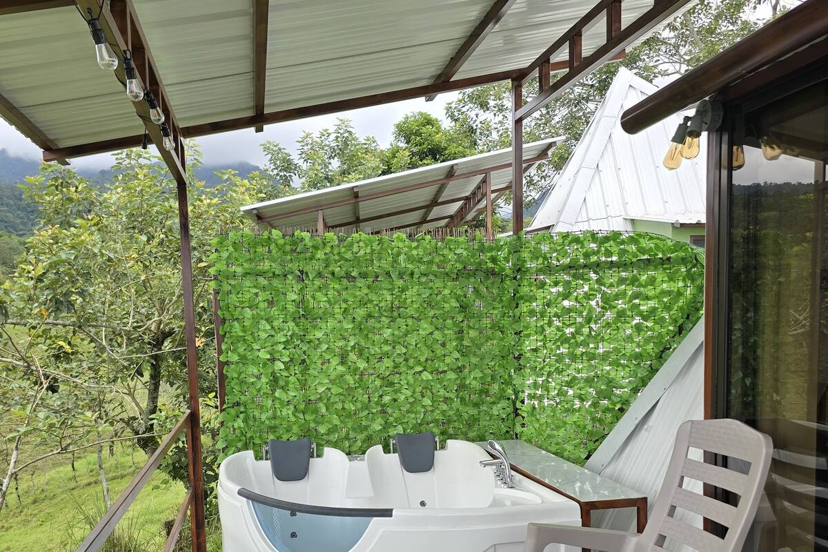Un espacio exterior techado con un jacuzzi, una mecedora y vistas de vegetación exuberante.