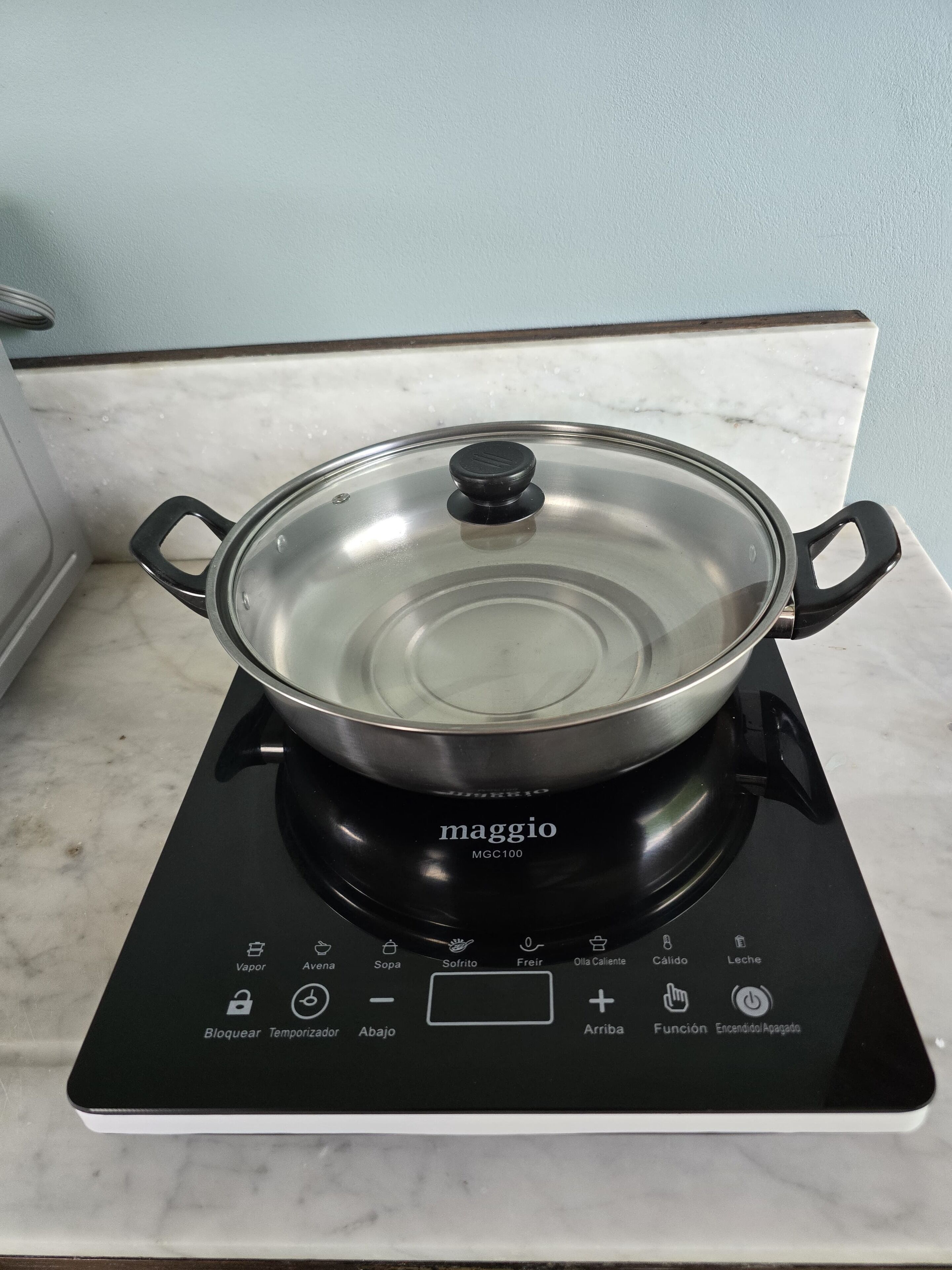 Une cuisine avec une plaque de cuisson à induction noire et une casserole en acier inoxydable posée dessus.