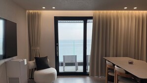 A modern hotel room with a balcony, a flat-screen TV, a compact sofa, a dining table, and a built-in air conditioning unit.