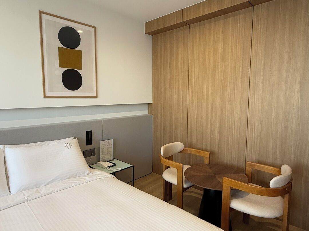 A hotel room with a bed, two chairs, a small table, a nightstand, and a framed picture on the wall.