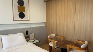 A hotel room with a bed, two chairs, a small table, a nightstand, and a framed picture on the wall.