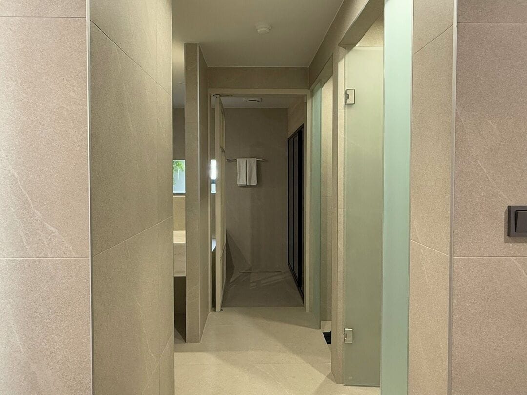 A modern hallway with a light-colored floor and walls, leading to a bathroom with a towel hanging on a rack.