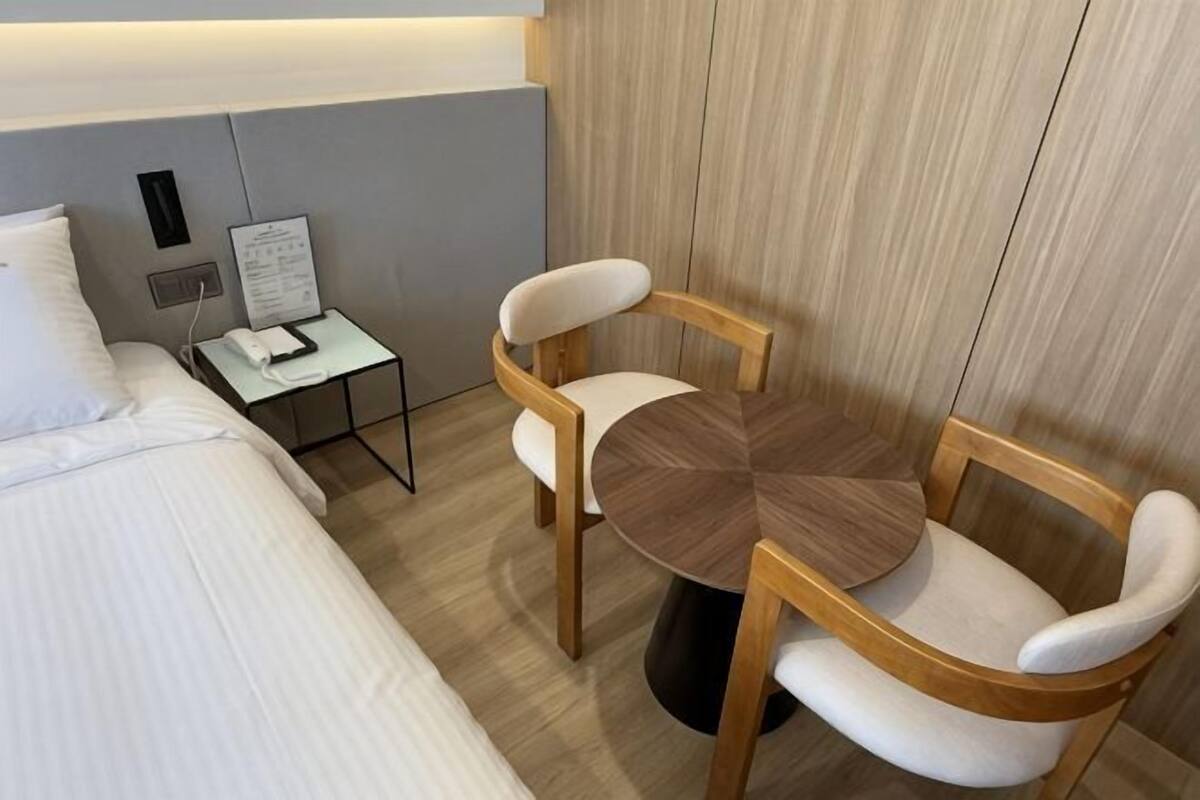 A hotel room with a bed, a small table with a chair, and a wooden table with two chairs.