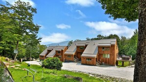 A row of wooden cabins with sloped roofs, set in a wooded area with a clear sky. - Trailside Village #1: Slopeside 1BR w/ Hot Tub and Sauna. Ski In/Out with Discounted Ski Rentals (Killington)