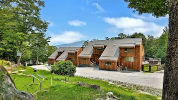 A row of wooden cabins with sloped roofs, set in a wooded area with a clear sky.