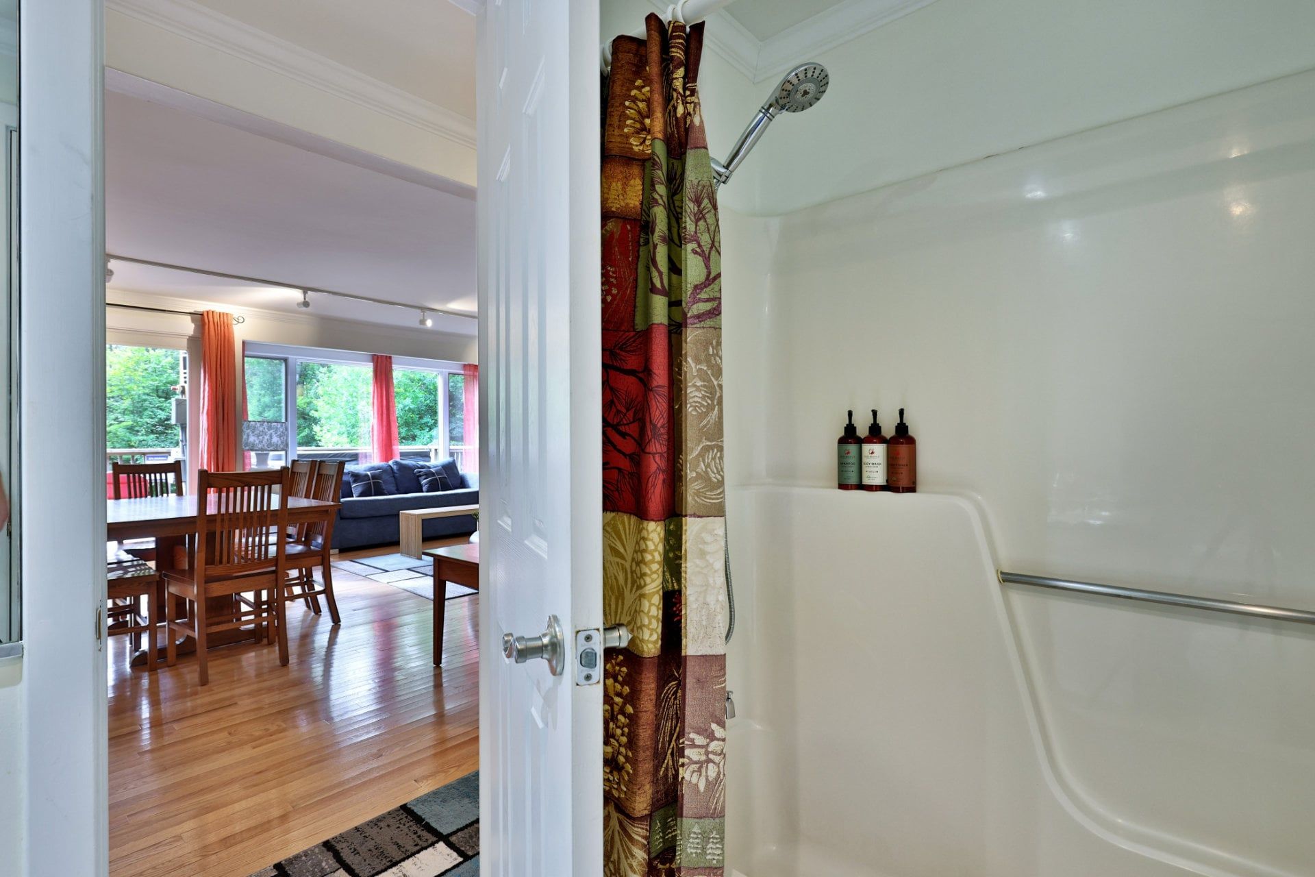 A bathroom with a shower, a toilet, and a sink. There is a window with curtains and a view of greenery outside.