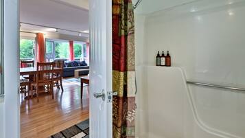 A bathroom with a shower, a toilet, and a sink. There is a window with curtains and a view of greenery outside.
