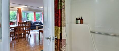 A bathroom with a shower, a toilet, and a sink. There is a window with curtains and a view of greenery outside.