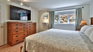 A bedroom with a bed, a wooden dresser, a television, and a window with curtains. - Trailside Village #1: Slopeside 1BR w/ Hot Tub and Sauna. Ski In/Out with Discounted Ski Rentals (Killington)