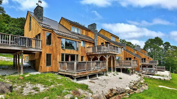 A wooden cabin with multiple balconies and a stone chimney. - Trailside Village #1: Slopeside 1BR w/ Hot Tub and Sauna. Ski In/Out with Discounted Ski Rentals (Killington)