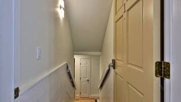 A narrow hallway with white walls, a door at the end, and a light fixture on the left.