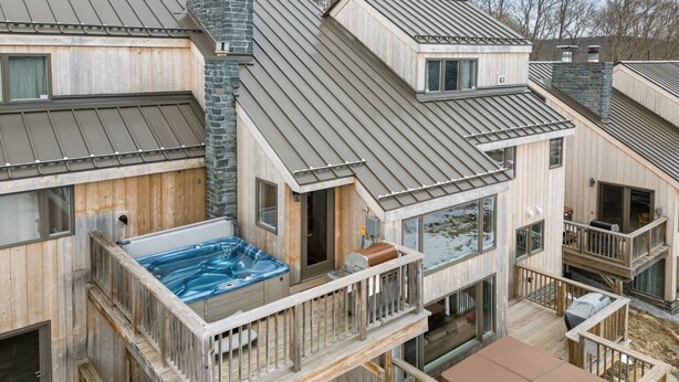 Eine mehrstöckige Holzhütte mit Whirlpool auf der zweiten Etage, Sitzgelegenheiten im Freien und einer Terrasse.