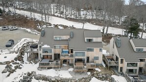 Ein modernes, mehrstöckiges Chalet mit Steinfundament, Holzterrassen und einer Skipiste im Hintergrund.