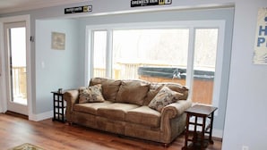 A living room with a beige sofa, two side tables, a patterned rug, and large windows with a view of a deck. - Trailside Village 3: Gas Fireplace, Hot Tub and Great Eastern Access (Killington)