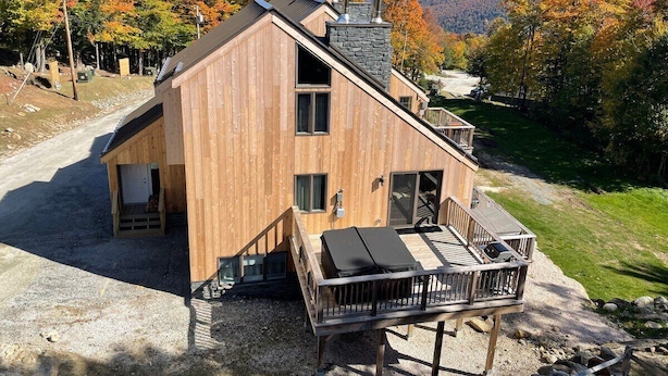 A wooden cabin with a balcony, a chimney, and a view of autumn trees. - Trailside Village 3: Gas Fireplace, Hot Tub and Great Eastern Access (Killington)