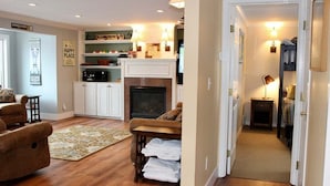 A cozy living room with a fireplace, a sofa, and a coffee table. There is a hallway leading to a bedroom with a bed and a nightstand. - Trailside Village 3: Gas Fireplace, Hot Tub and Great Eastern Access (Killington)