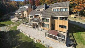 A modern multi-story building with a stone foundation, wooden exterior, and multiple balconies with outdoor seating. - Trailside Village 3: Gas Fireplace, Hot Tub and Great Eastern Access (Killington)