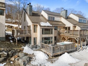 A wooden cabin with multiple decks and large windows, surrounded by snow and rocks. - Trailside Village 5: Wood Stove, Private Sauna and Hot Tub (Killington)