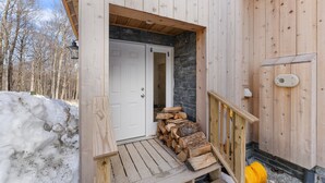 A wooden cabin with a white door, a stone wall, and a wooden staircase leading to a deck. - Trailside Village 5: Wood Stove, Private Sauna and Hot Tub (Killington)
