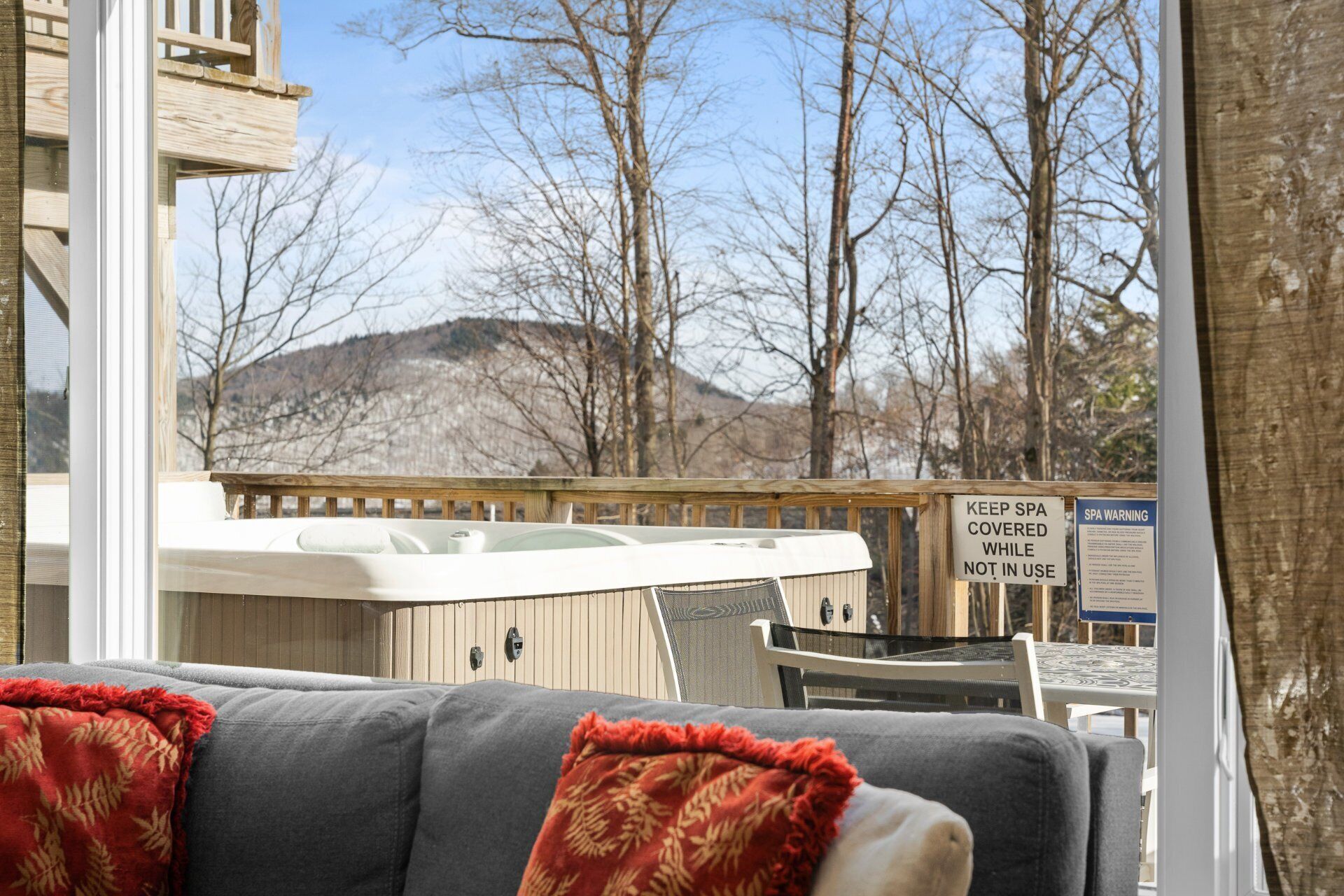 Un espace de détente aménagé, abrité, avec un jacuzzi, un coin salon couvert et une vue sur les arbres et les collines.